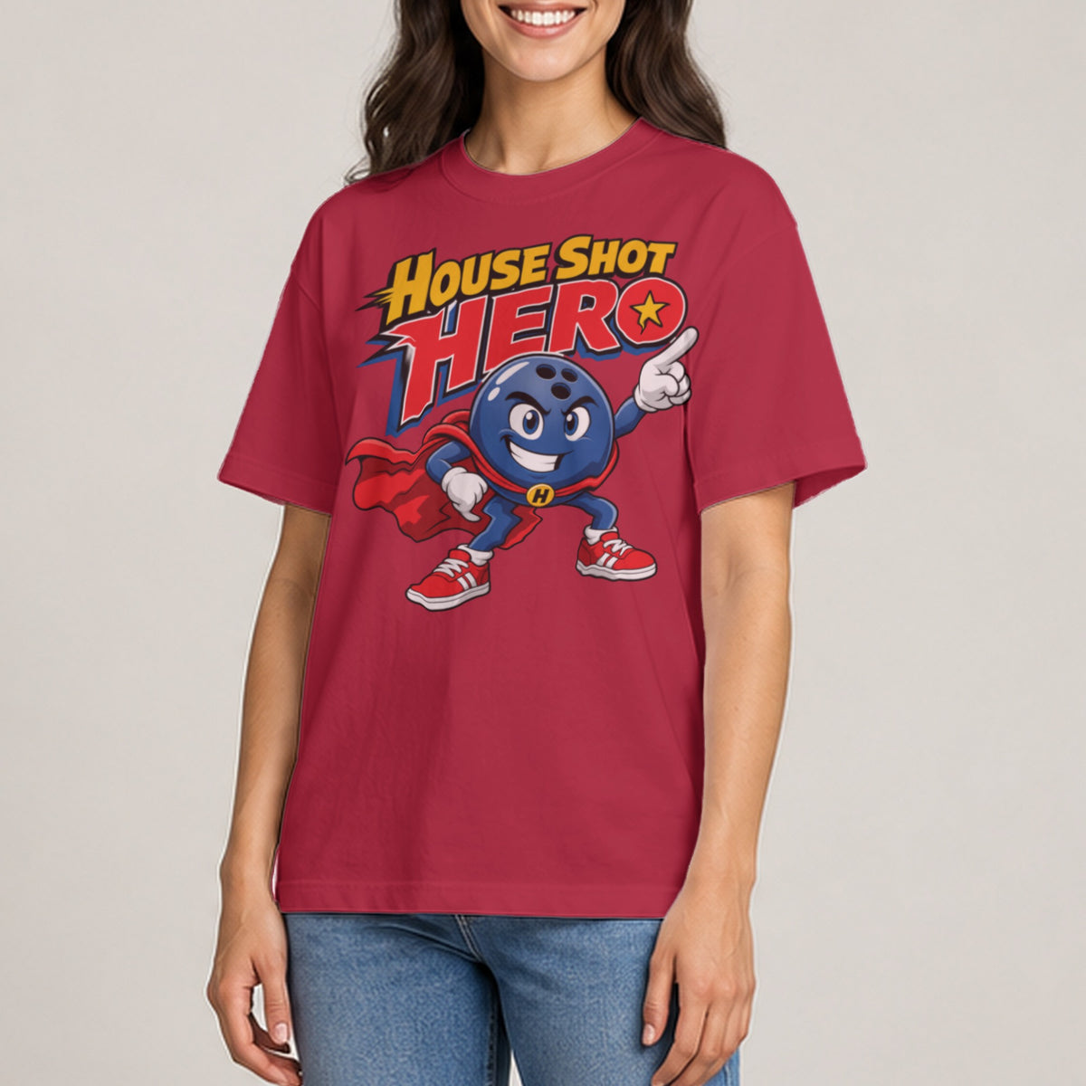 A person wearing a red t-shirt printed with a cartoon bowling ball superhero character and the text House Shot Hero.